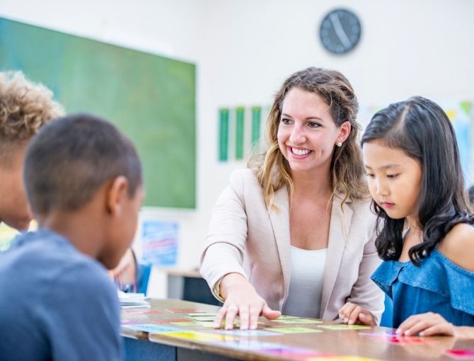 Teacher in focus moving colorful review cards on a desk with three students 