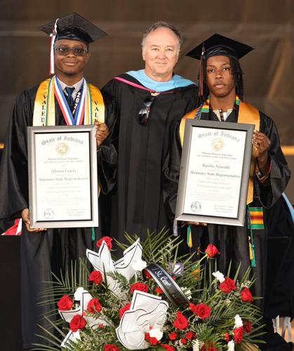 Two students in graduation caps and gowns with diplomas with adult in the center