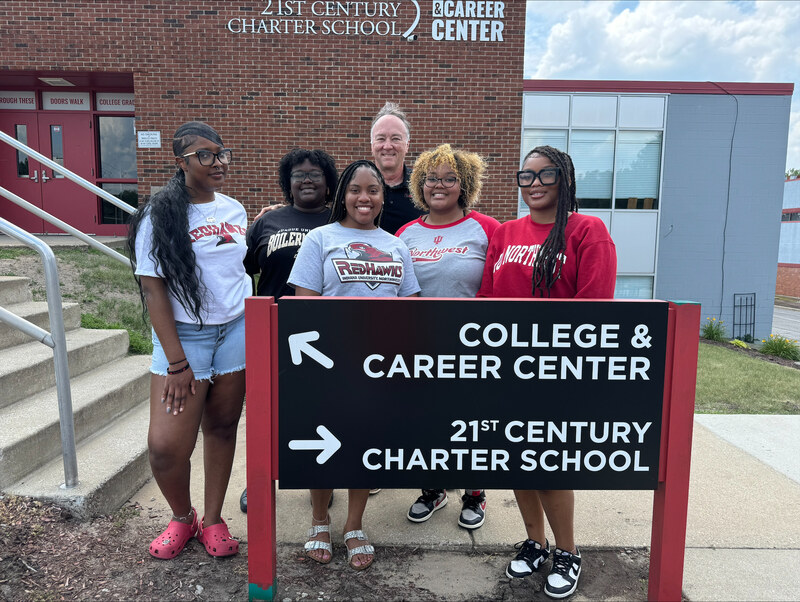 Five students and one adult in front of a 21st Century Charter School sign
