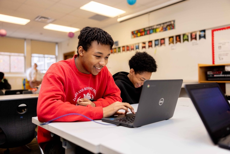 Student smiling with one hand on laptop