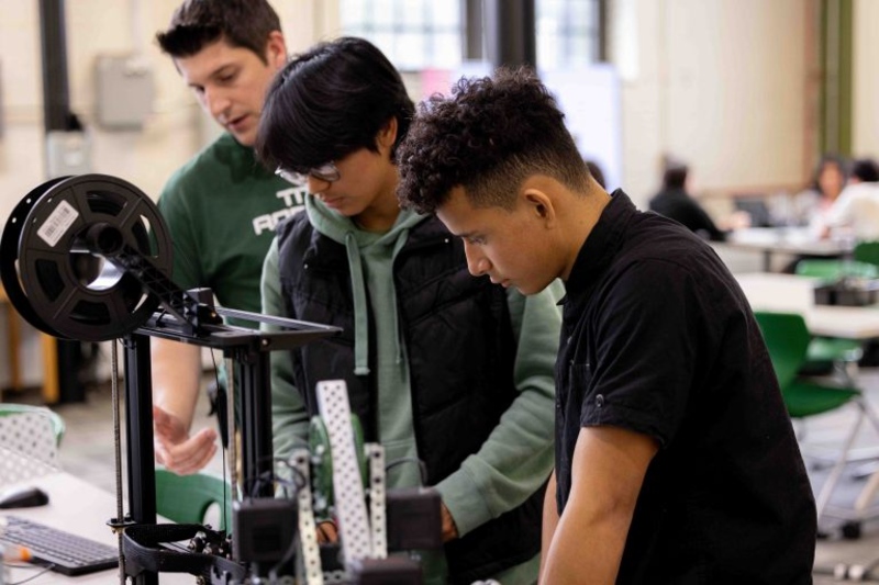 Three students leaning over machine