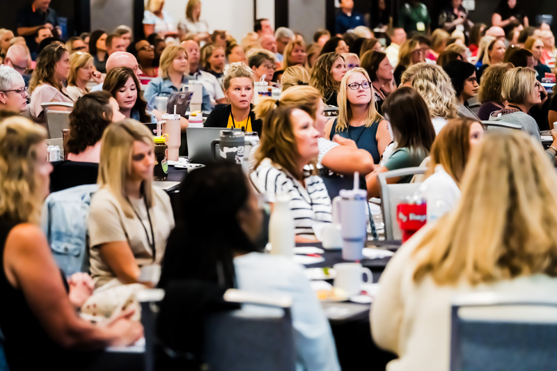 Large conference audience seated at tables, listening attentively during a presentation.