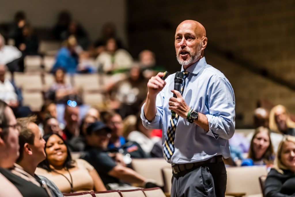 Person speaking with microphone with audience in background
