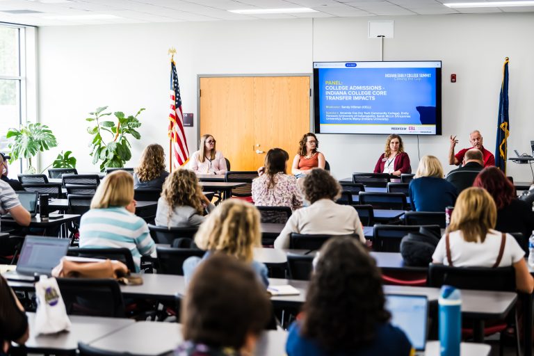 Panelists speaking in front of room with people seated at desks