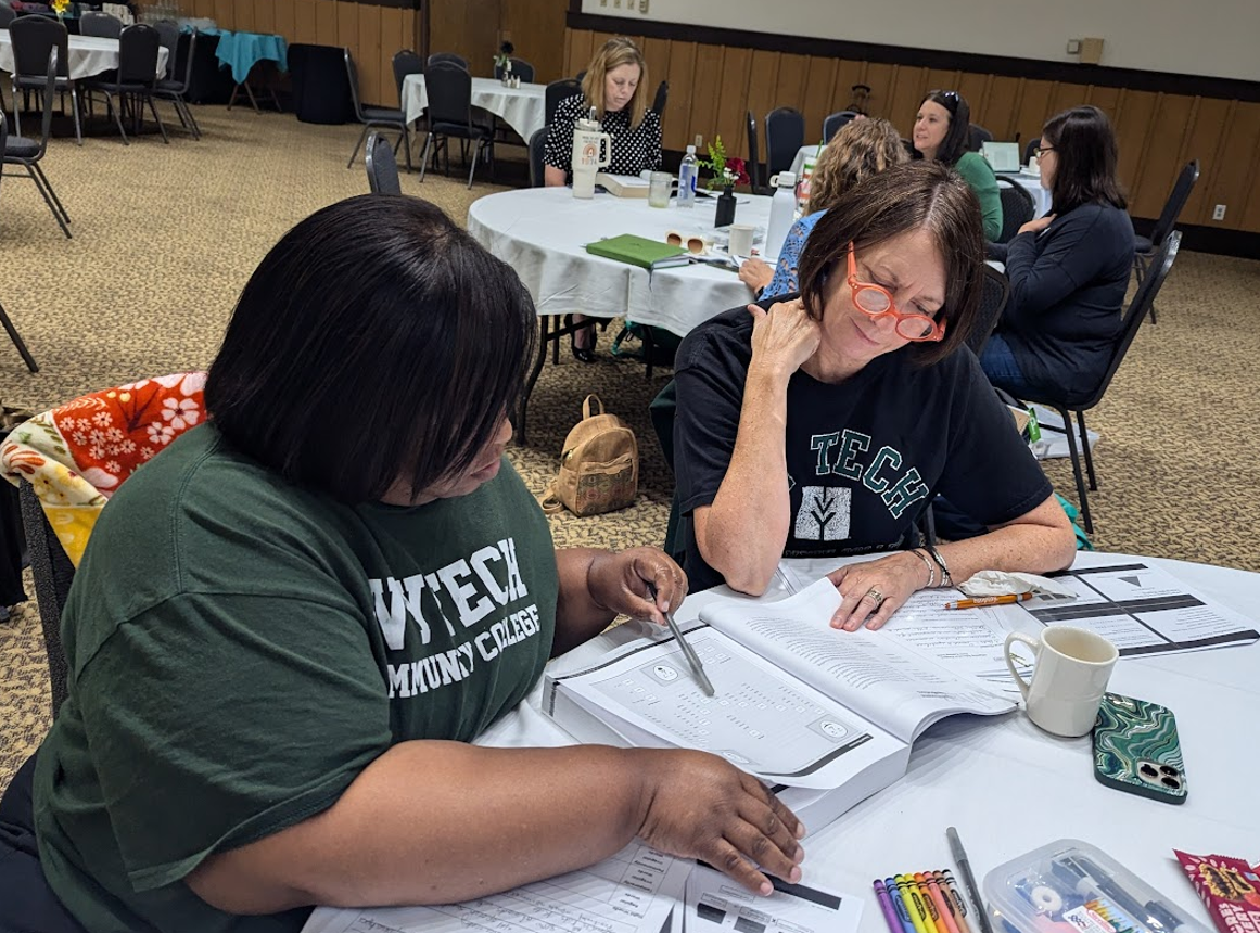 Two educators look at a workbook at a table