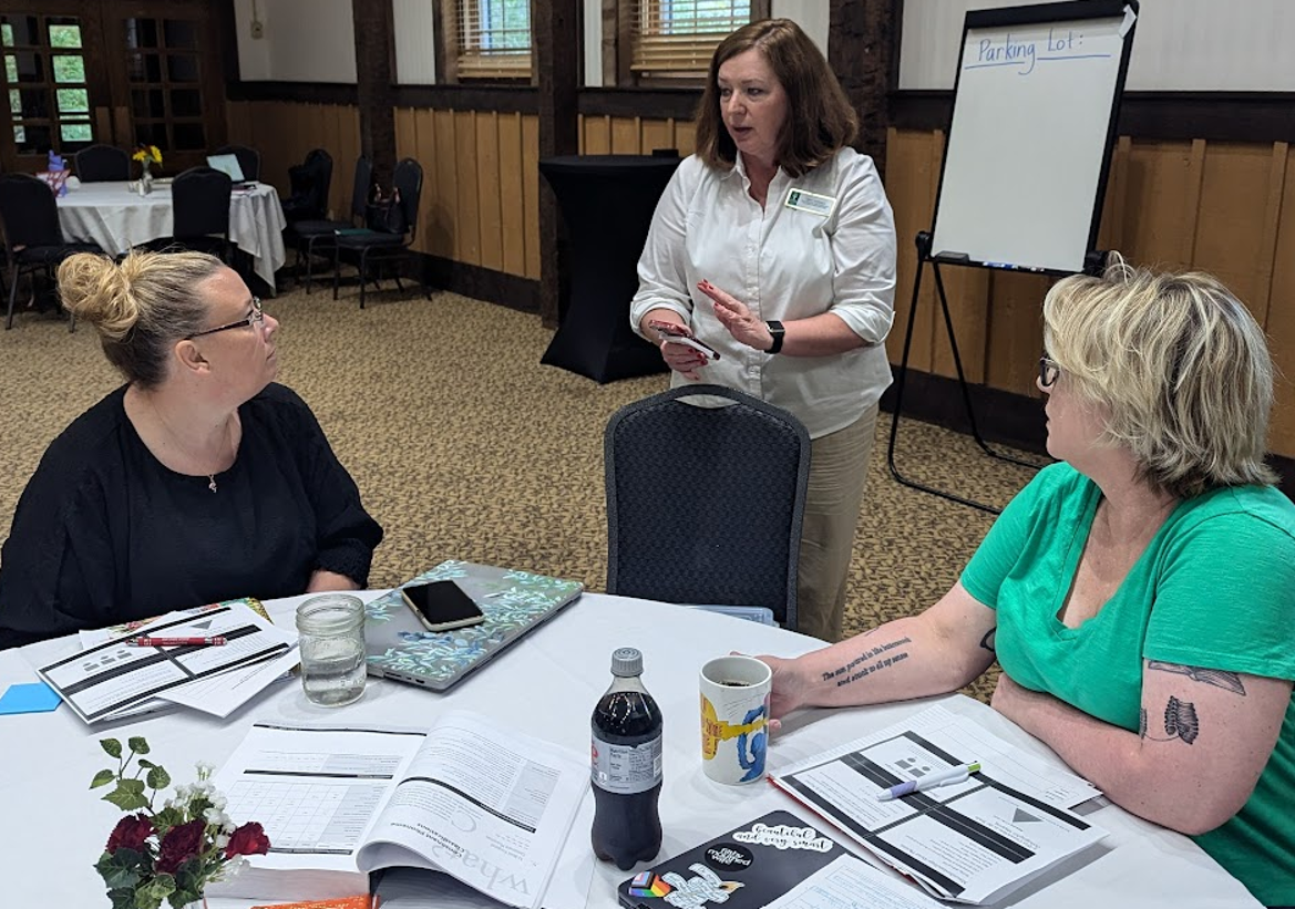 Person standing explaining something to two people seated at tables