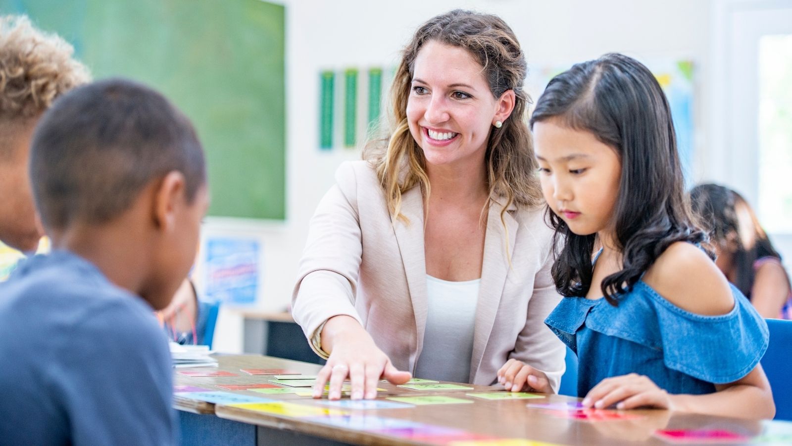 Teacher in focus moving colorful review cards on a desk with three students 