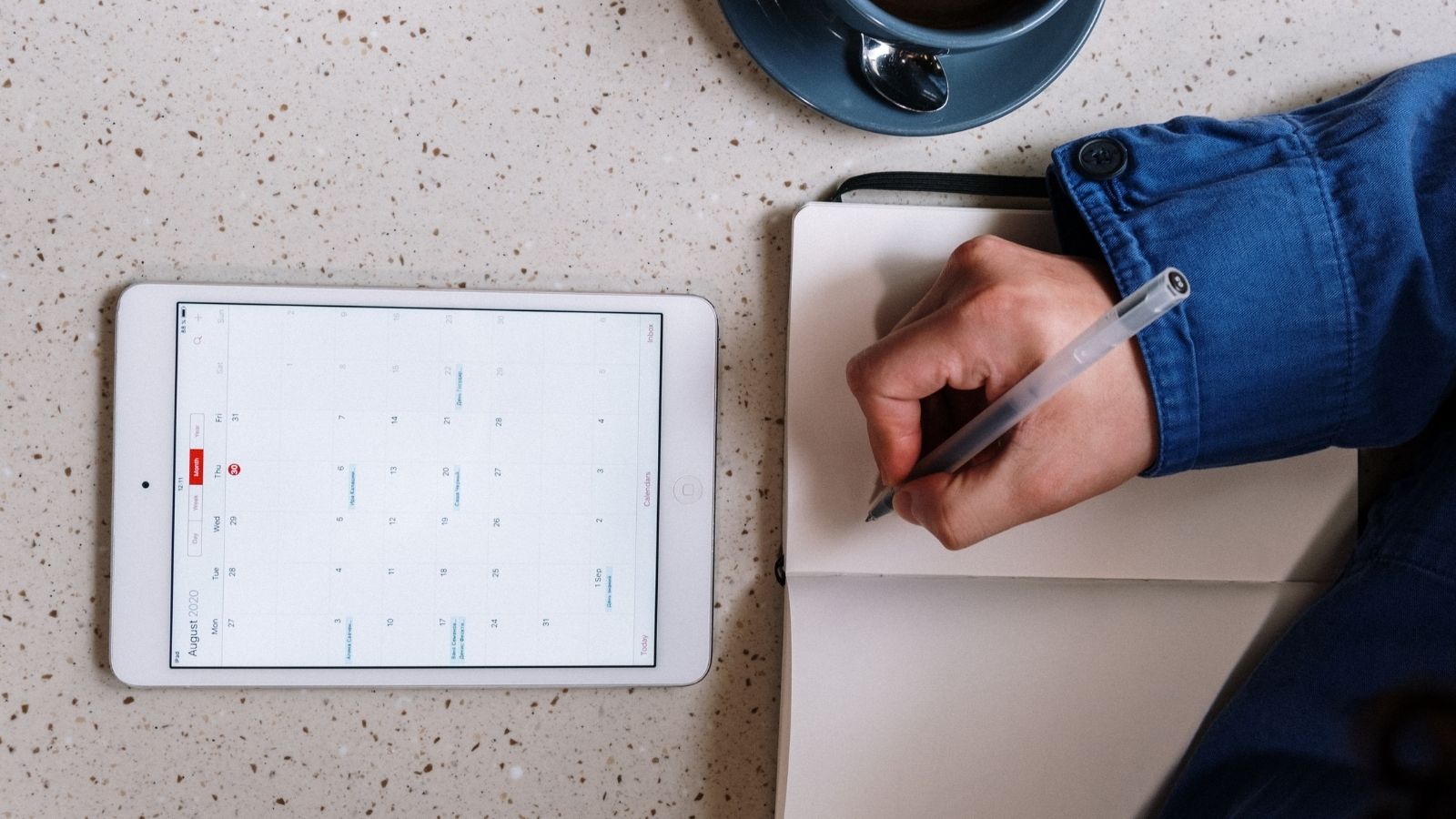 Person holding pen over journal with tablet and calendar